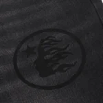 Close-up view of the Hellstar brand logo embroidered on the black washed premium denim fabric of the Hellstar jeans.