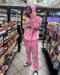 A person standing in a store wearing a stylish pink Hellstar Brainwashed hoodie and matching graphic sweatpants.