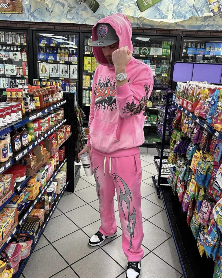 A person standing in a store wearing a stylish pink Hellstar Brainwashed hoodie and matching graphic sweatpants.