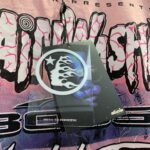 Detail of the pink Hellstar Brainwashed World Tour T-shirt featuring a hanging brand tag and vintage-washed graphic print.