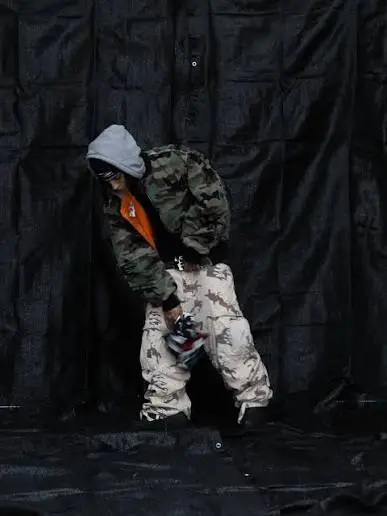 Person wearing a Hellstar camo jacket and baggy pants with a grey hoodie against a black background