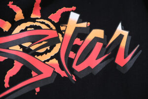 Detailed close-up view of the Hellstar Capsule 8 black t-shirt featuring a vibrant orange and red sun graphic print.