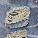 Close-up view of the distressed fabric texture and frayed hole details on Hellstar Capsule 9 blue denim shorts.