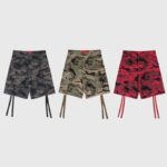 Three pairs of Hellstar cargo shorts in brown, green, and red camouflage prints with hanging straps and pocket details.