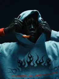 A model wearing a stylish Hellstar graphic print hoodie with a flame design pulled over their head in a dark studio.