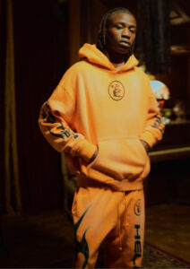 A model wearing the Hellstar Fire Orange Dye Tracksuit featuring a vibrant vintage-washed orange hoodie and sweatpants.