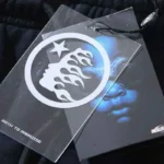 Close-up view of the Hellstar brand hang tag featuring the signature flame logo on the black streetwear sweatpants.