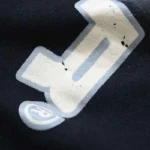 Close-up view of the distinctive white graphic logo detail on the black Hellstar Flame sweatpants fabric.