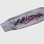 Close-up view of a grey Hellstar Future Flame hoodie sleeve featuring bold pink and black flame graphic branding.