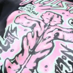Close-up of Hellstar Guts Glory hoodie pink and mint graphic print on black fleece showing bold screen-printed artwork