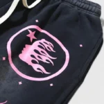 Close-up of black Hellstar Guts Glory tracksuit pants featuring a pink circular logo with flame and star graphics.