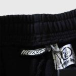 Hellstar Hstar shorts authenticity tag detail showing the premium brand label and NFC verification tag on black fleece.