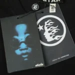 Close up of the Hellstar Lens of Honesty T-shirt branding tags featuring an eye graphic and Path to Paradise logo.