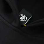 Close-up view of the interior neck tag detail on a black Hellstar Mask Print Hoodie showing the brand logo design.