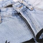 Close-up view of a Hellstar men’s light blue vintage washed denim jean featuring a button and zipper closure detail.