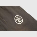Close-up view of brown Hellstar Mirror Faced sweatpants featuring a signature white flame graphic print detail.