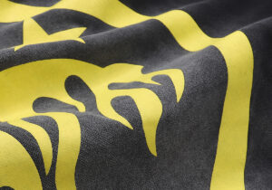 Close up texture view of the black Hellstar No Guts No Glory hoodie with yellow graphic print details and fabric folds.
