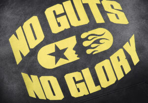 Close-up graphic detail of the Hellstar No Guts No Glory washed black hoodie featuring yellow screen print text.