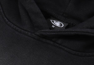 Detail of the branded Hellstar clothing label inside the collar of a black No Guts No Glory cotton fleece hoodie.