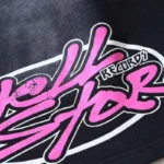Close-up view of the bold pink logo graphic printed on the black cotton fabric of Hellstar No Humanity shorts.