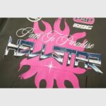 Hellstar Path To Paradise hoodie featuring a bold pink sun graphic and retro logo print on dark green fabric.