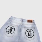Back view of light blue Hellstar loose denim jeans featuring a circular graphic flame logo on back pockets.