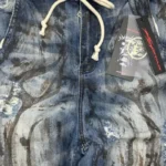 Close-up of Hellstar raw edge jeans showing the branding tag and washed blue denim fabric with distressed details.