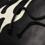 Close up of black Hellstar Sports Flame shorts with white flame graphic design and black drawstring adjustment cords.