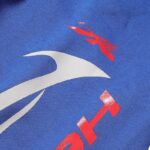 Close-up view of the Hellstar Sports Gel blue sweatpants fabric featuring vibrant red and white graphic logo details.