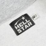 Close-up view of the black and white Hellstar Sports branding label stitched onto the grey cotton fabric sweater.