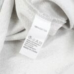 Close-up of Hellstar Sports grey sweatpant fabric care tag reading "100% COTTON" with washing symbols on textured fleece