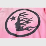 Close-up view of the black Hellstar Studios logo graphic print on a pink vintage washed zip-up streetwear hoodie.