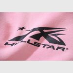 Close-up of the iconic black Hellstar Studios logo screen-printed on a soft pink zip-up hoodie fabric.