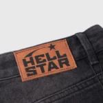 Brown leather branding patch with the Hellstar logo stitched on black denim streetwear jeans