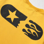 Close-up of a Hellstar Sports yellow sweatshirt featuring a black graphic with a star and flame design.
