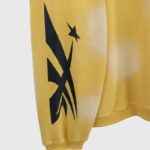 Close-up of the Hellstar Sports yellow sweater sleeve showing the black star-inspired graphic and ribbed cuff detail.