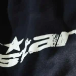 Close-up view of the white graphic screen print logo on black Hellstar Studio fleece shorts fabric.