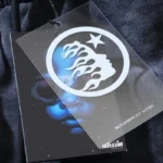 Close-up view of the Hellstar Studios branding tag featuring a circular logo and graphic on a washed grey fabric tracksuit.