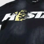 Close-up view of a black Hellstar Studios graphic t-shirt featuring a distressed white and yellow cartoon logo design.