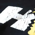 A detailed close-up of the distressed white cartoon graphic logo printed on a black Hellstar Studios cotton T-shirt.