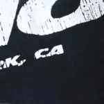 A closeup view of the white graphic print on a black Hellstar Studios cartoon logo cotton t-shirt for men.