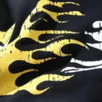Close-up view of the bold yellow and white cartoon graphic print featured on the black Hellstar Studios logo t-shirt.