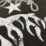 Close-up view of the white graphic screen print on a black Hellstar Studios Chrome Logo cotton T-shirt fabric.