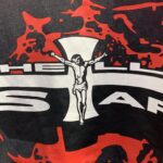 Close-up graphic of the Hellstar Studios Jesus emblem featuring a cross design on a black t-shirt with red accents.