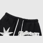 Close-up view of the elastic drawstring waistband and iconic graphic screen print on black Hellstar Studios Racer sweatpants.