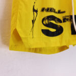 Side view of yellow Hellstar Studios Records Star shorts featuring black distressed screen-printed graphic logo details.