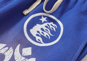 Close-up of the graphic logo on blue Hellstar Studios Records yoga sweatpants featuring a white star and flame design.