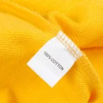 Close up view of the 100% cotton material tag on the vibrant yellow Hellstar Studios zipper sweater fabric.