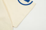 Close-up view of the beige Hellstar Studios Yoga T-Shirt sleeve showing the blue graphic print detail and fabric.