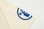 Close-up of the beige Hellstar Studios Yoga T-Shirt sleeve featuring a circular blue graphic print and star logo.